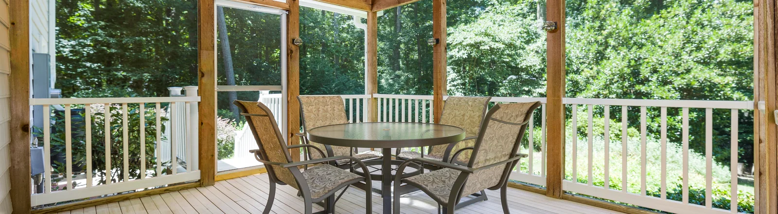 Helle überdachte Holzveranda mit Tisch, Sesseln und Blick in einen grünen Garten